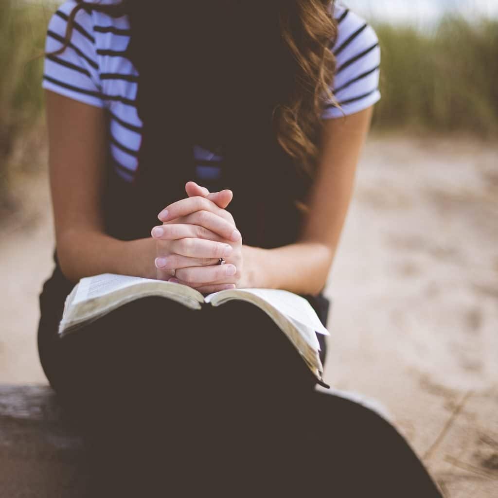Girl sitting down reading the Bible and praying