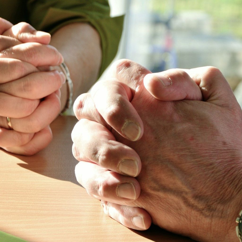 Two people sitting with their hands crossed praying