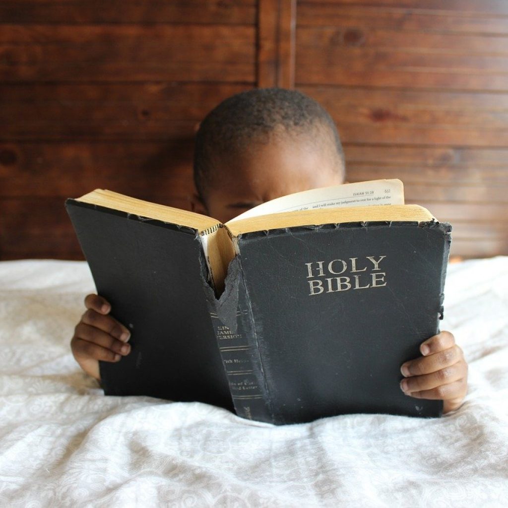 Bambino che legge la Bibbia sul letto