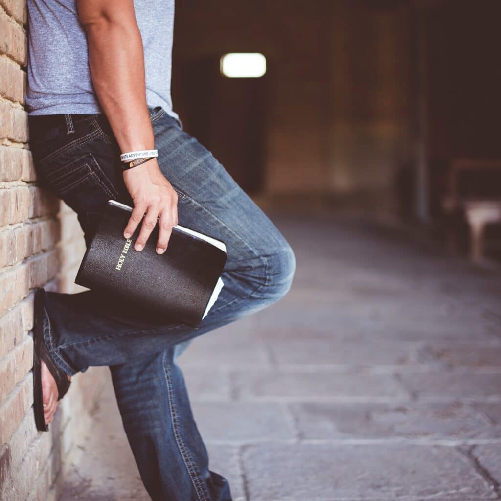 Person leaning on wall with Bible in his hand